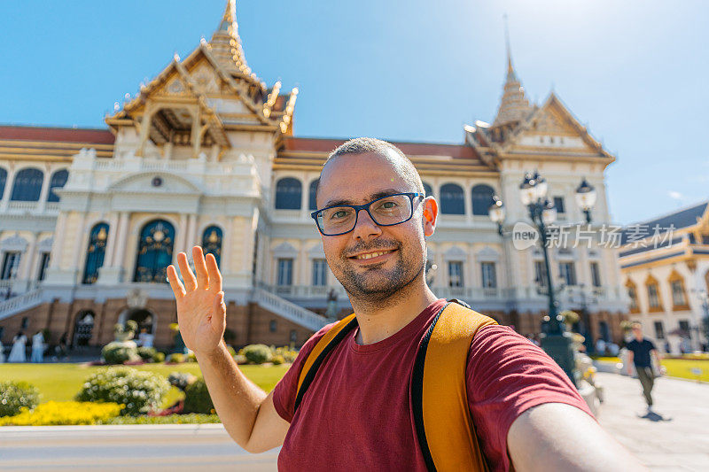 在泰国曼谷大皇宫建筑群的Chakri Maha Prasat王座大厅进行视频通话的年轻人